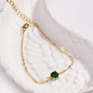 Detailed close-up of a delicate gold chain bracelet featuring a round green gemstone inlay