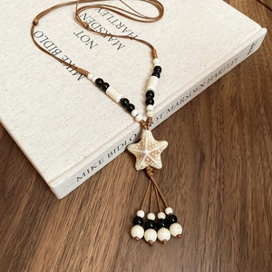 Close-up of ceramic starfish pendant with woven rope and beads on a vintage book