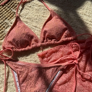 Detail of coral lace bikini with metal charm and matching mesh beach skirt