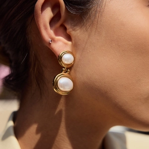 Close-up of model wearing elegant gold earrings with double pearls in natural outdoor light