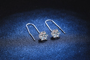 Macro close-up of S925 sterling silver six-prong moissanite drop earrings on blue background