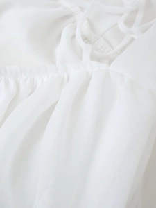 Macro detail of white chiffon dress showing pleated chest texture and thin lace-up back straps