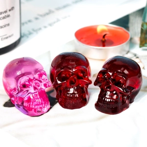 Detailansicht von drei Totenkopf-Figuren aus Harz in Rot und Lila mit Kerzen