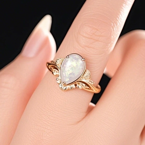 Close-up of a pear-shaped opal ring with vintage gold leaf textures on a finger