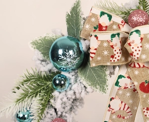 Macro detail of flocked pine wreath featuring blue glitter ornaments and snow pattern ribbon