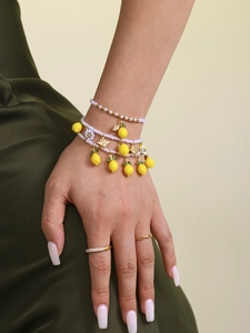 Close-up of layered pearl bracelets with lemon and daisy charms on green satin fabric