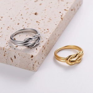 Polished gold and silver knot rings on a beige stone platform for a minimalist look