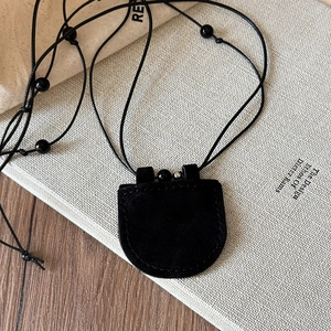 Detail of a vintage black faux leather magnetic glasses holder pendant on a suede necklace