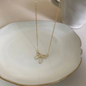 Detailed view of a gold bow pendant necklace with zircons resting on a ceramic plate