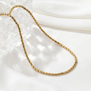 Close-up of golden cylindrical bead necklace on glass edge with white satin fabric