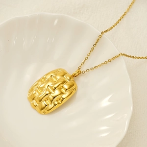 Detail shot of golden textured rectangular pendant and chain on a shell tray