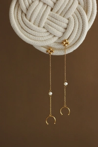 Detail of clover tassel earrings featuring white pearls and gold chains on a warm backdrop