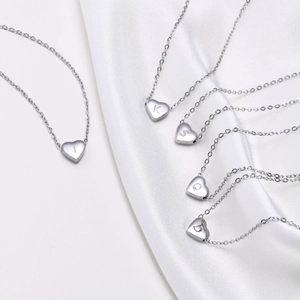 Macro shot of silver heart-shaped alphabet necklaces on white silk fabric background