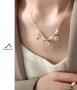 Detail showing an evil eye pendant necklace with pearls and matching gold ring on model