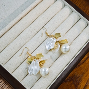Detail of star-shaped charms and white pearl petals on elegant hook earrings