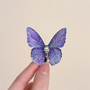 Macro detail of a purple resin butterfly hair clip with gold foil and a pearl pendant