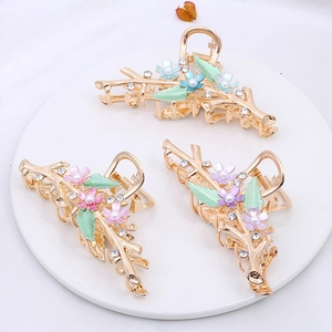 Detail of three alloy hair claws with enamel flowers, pearls and rhinestones on white plate