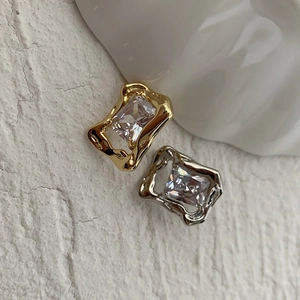 Macro detail of geometric zircon earrings with molten metal frames on white textured surface