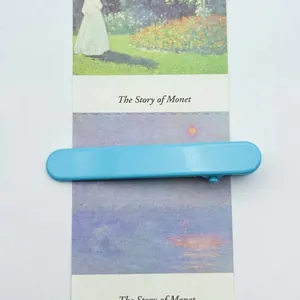 Detail view of a slim light blue matte alligator hair clip on a vintage Monet card