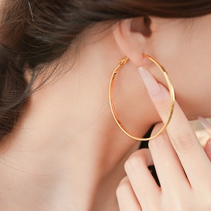Close-up of model wearing large geometric gold hoop earrings with polished metal finish