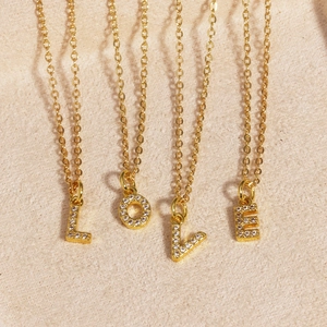 Detail of gold LOVE letter necklaces with sparkling zircon stones on beige velvet