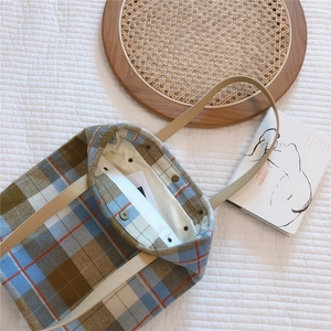 Plaid canvas tote bag detail showing metal snap closure and textured plaid fabric