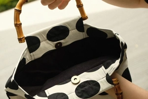 Detail view of the bamboo handle and magnetic closure on a polka dot canvas handbag