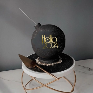 Close-up of black bomb-shaped cake with gold Hello 2024 text and sparkling sand effect
