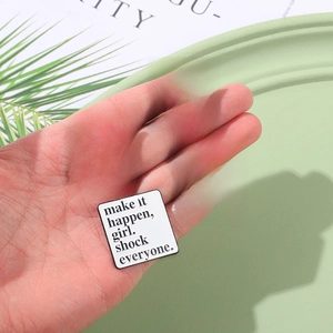 Square enamel motivational brooches featuring black text on white metal base held by hand