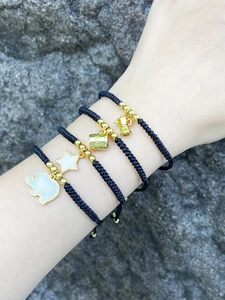 Detalle de cuatro pulseras tejidas negras hechas a mano con dijes de elefantes dorados
