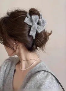 Detail of grey knitted bow hair claw clip styled on a woman's hair with a soft winter vibe