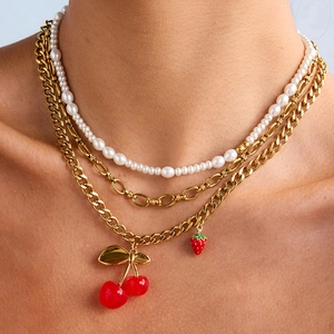 Close-up of layered gold chain necklace featuring red cherry and strawberry charms with pearls