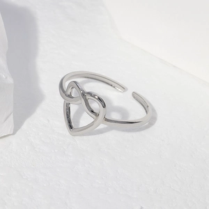 Close-up of silver stainless steel heart knot open ring on textured stone surface