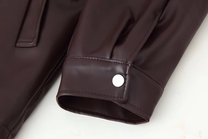 Detailed close-up of dark brown faux leather jacket sleeve with silver snap button
