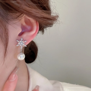 Close-up of elegant snowflake zircon earrings with white pearl pendants on model