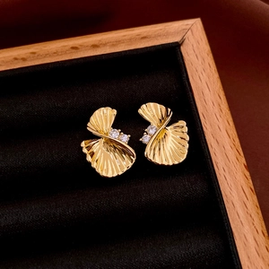 Macro shot of gold fan-shaped stud earrings with zircon inlay on black velvet tray
