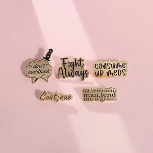 Set of five motivational enamel pins with gold finish and black inscriptions on pink surface