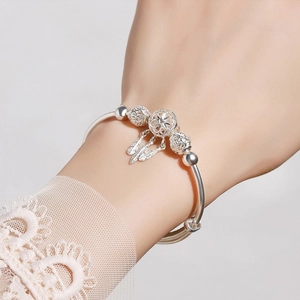 Detail of silver dreamcatcher bracelet featuring delicate feather pendants and hollow beads