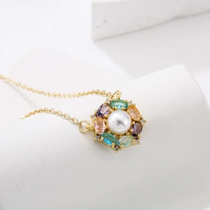 Gold necklace with pearl flower pendant and colorful gemstones on white geometric base