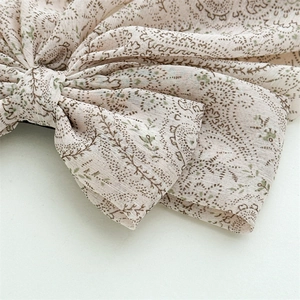 Close-up of beige fabric bow hair clip featuring detailed brown and green paisley patterns