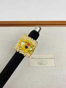 Detailed view of a square gold ring with white pearls and a colorful eye motif