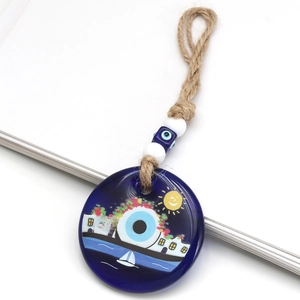 Close-up of blue glass evil eye pendant with seaside house and sailboat painting