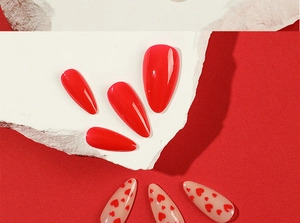 Detail of red and nude almond press-on nails with heart patterns on stone display