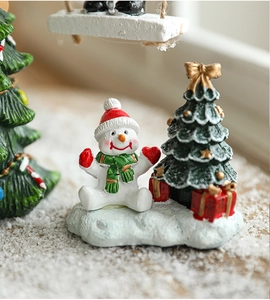 Miniature resin snowman and Christmas tree scene on artificial snow for holiday decor