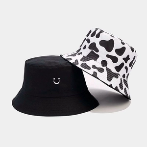 Detail showing a black bucket hat with smiley embroidery and a cow print pattern hat