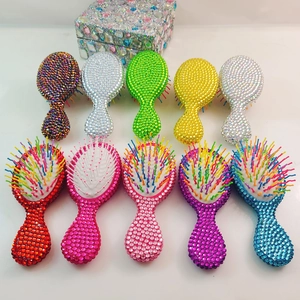 Detailed view of ten colorful rhinestone-studded mini hairbrushes on a white surface