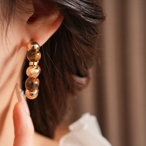 Primer plano de pendientes de aro C con ojo de tigre y perlas en estilo vintage