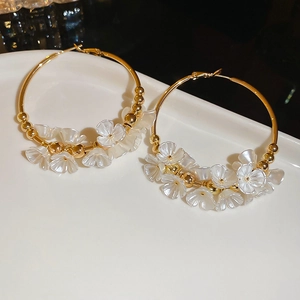 Macro shot of gold hoop earrings with white acrylic flowers and beads on a tray