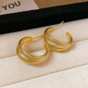 Macro detail of gold C-shaped hoop earrings featuring multi-layered grainy vintage textures