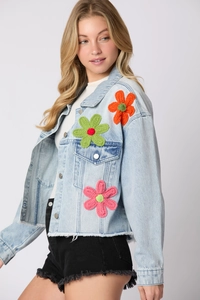 Detail of light blue denim jacket featuring colorful 3D crochet floral embellishments